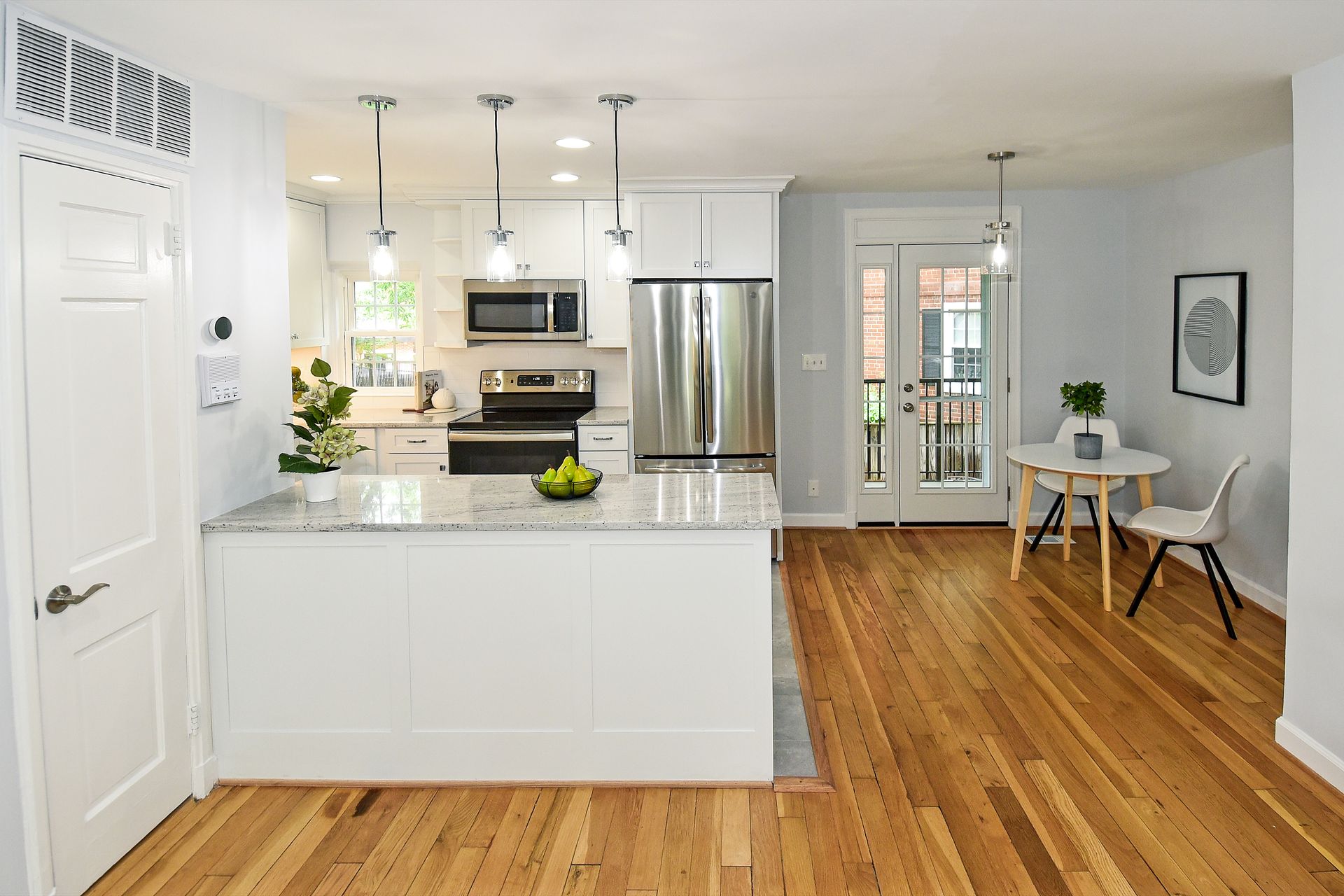 A kitchen with hardwood floors , white cabinets , stainless steel appliances and a large island.
