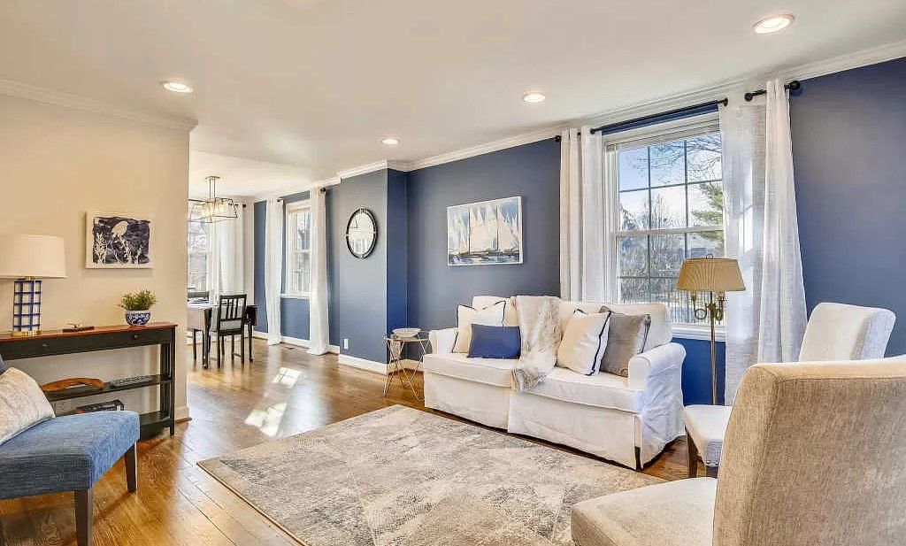A living room with blue walls , white furniture , and a rug.