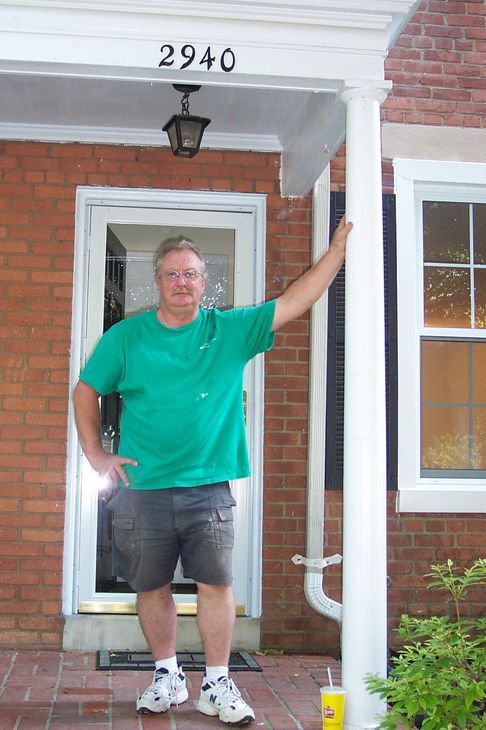 A man in a green shirt is standing in front of a house with the address 2940