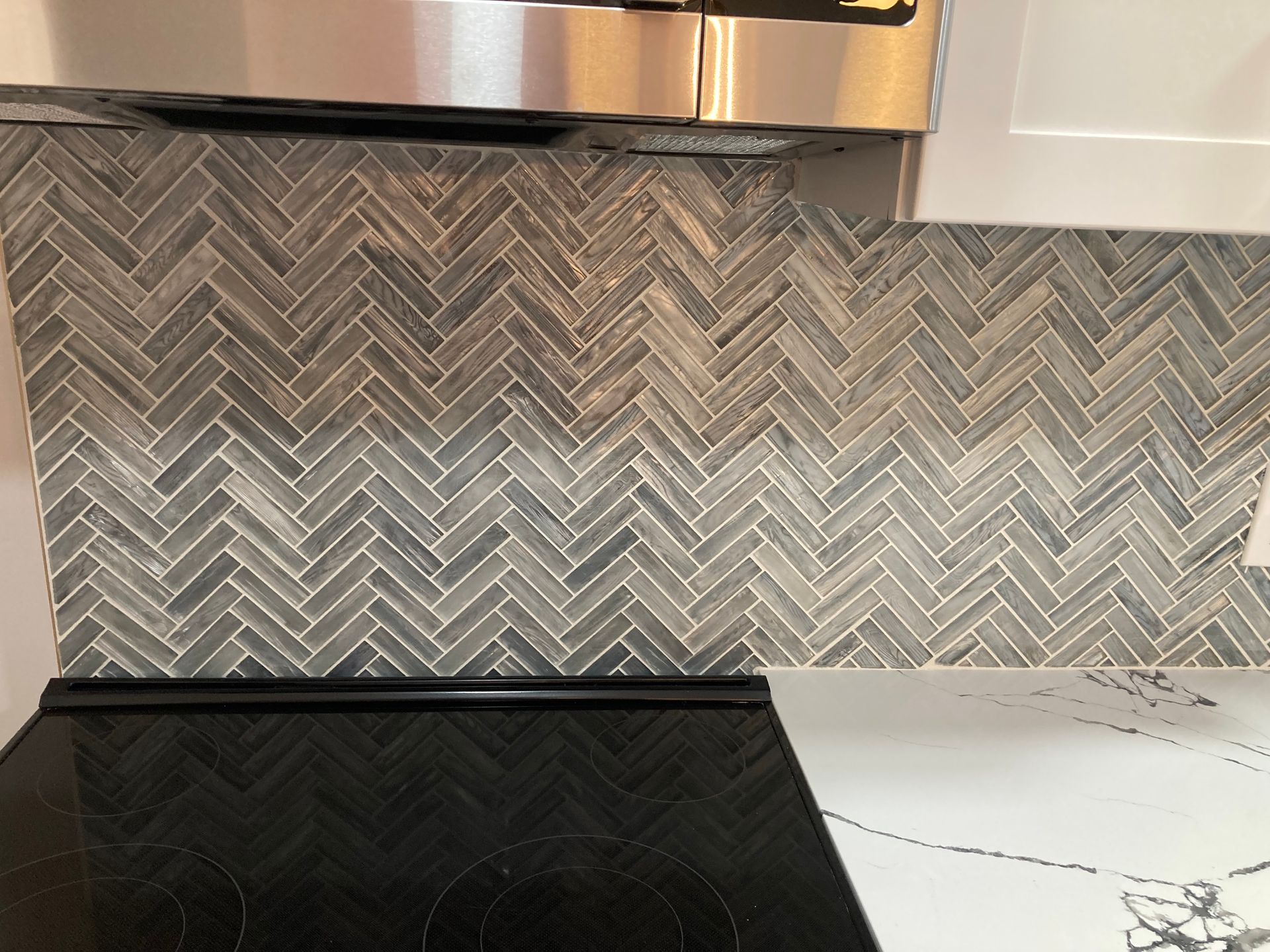 A kitchen with a black stove top oven and a herringbone tile wall.