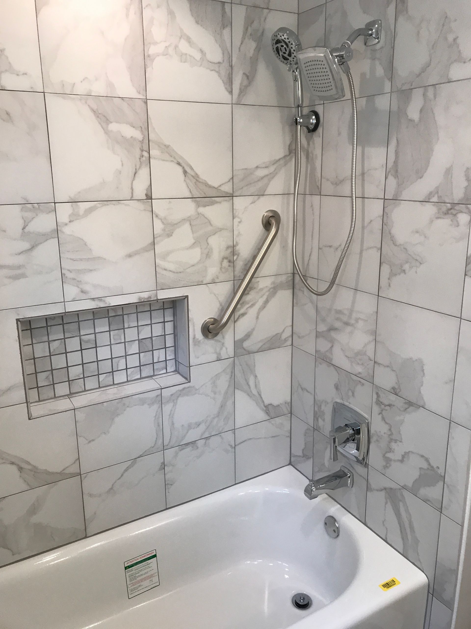A bathtub in a bathroom with marble tiles and a shower head.