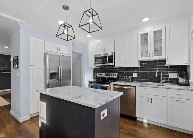 A kitchen with white cabinets , stainless steel appliances , and a large island.