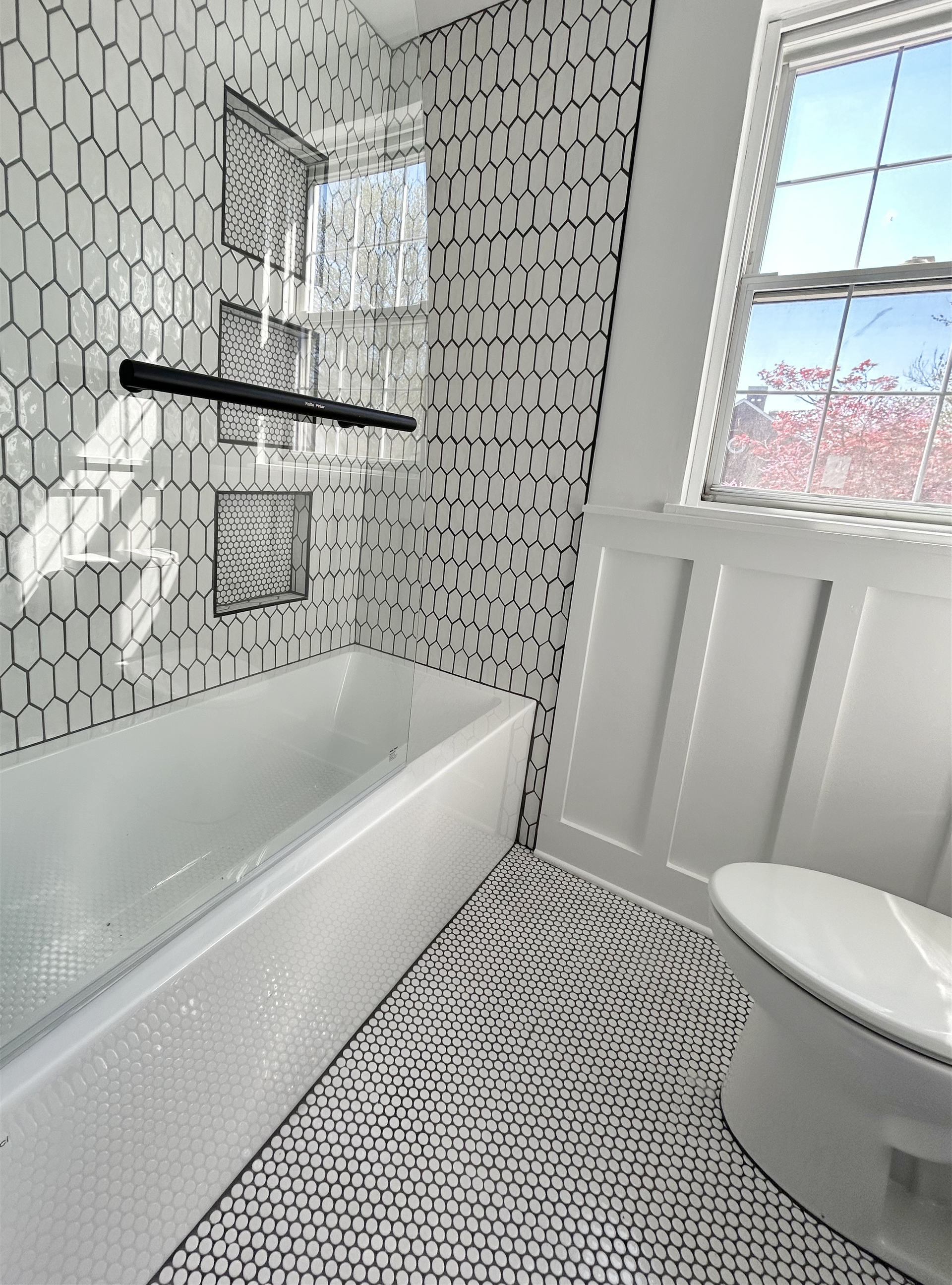 A bathroom with a tub , toilet , shower and window.