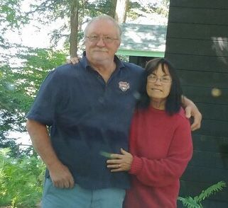 A man and a woman are posing for a picture . the woman is wearing a red sweater.