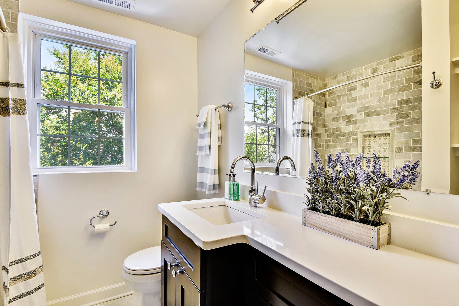 A bathroom with a sink , toilet , mirror and window.