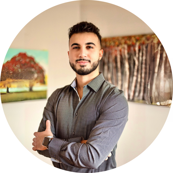 Headshot of Therapist Nadeem: Smiling warmly in a professional office with paintings of trees in the background.