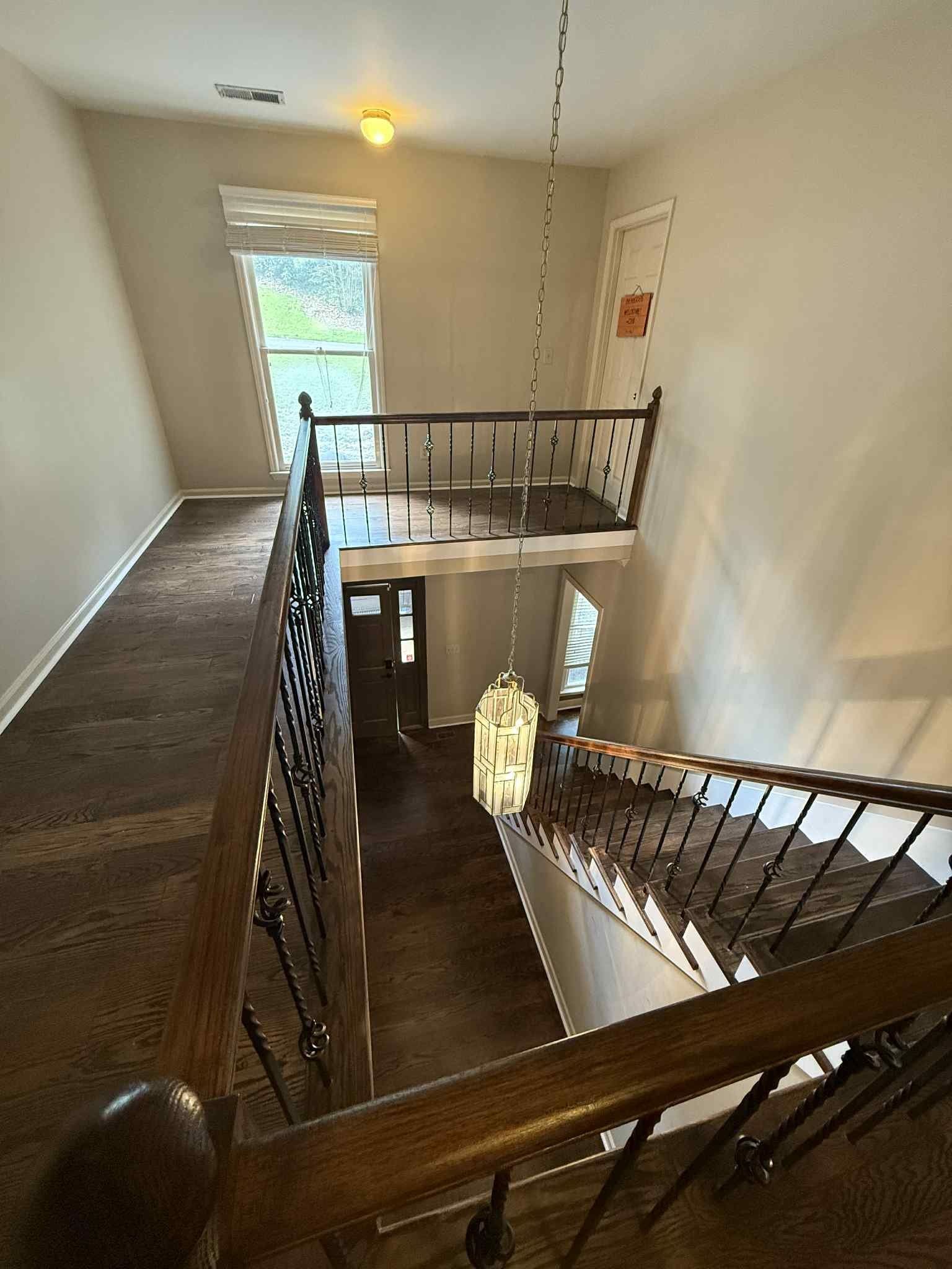 View from top of stairs. Brown staircases and flooring with white walls and a chandelier.