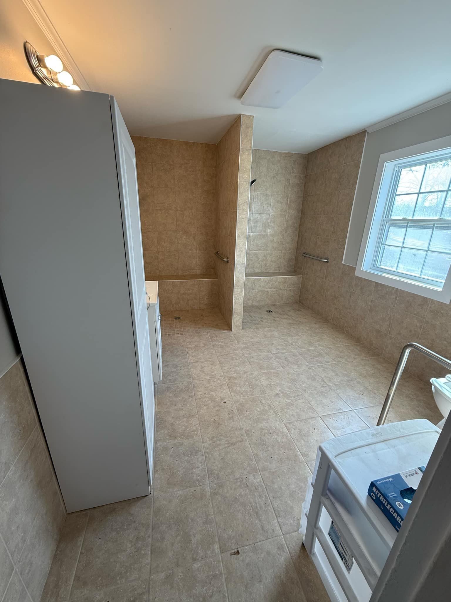 Bathroom with beige tile walls and floor, a white cabinet, and a small window.
