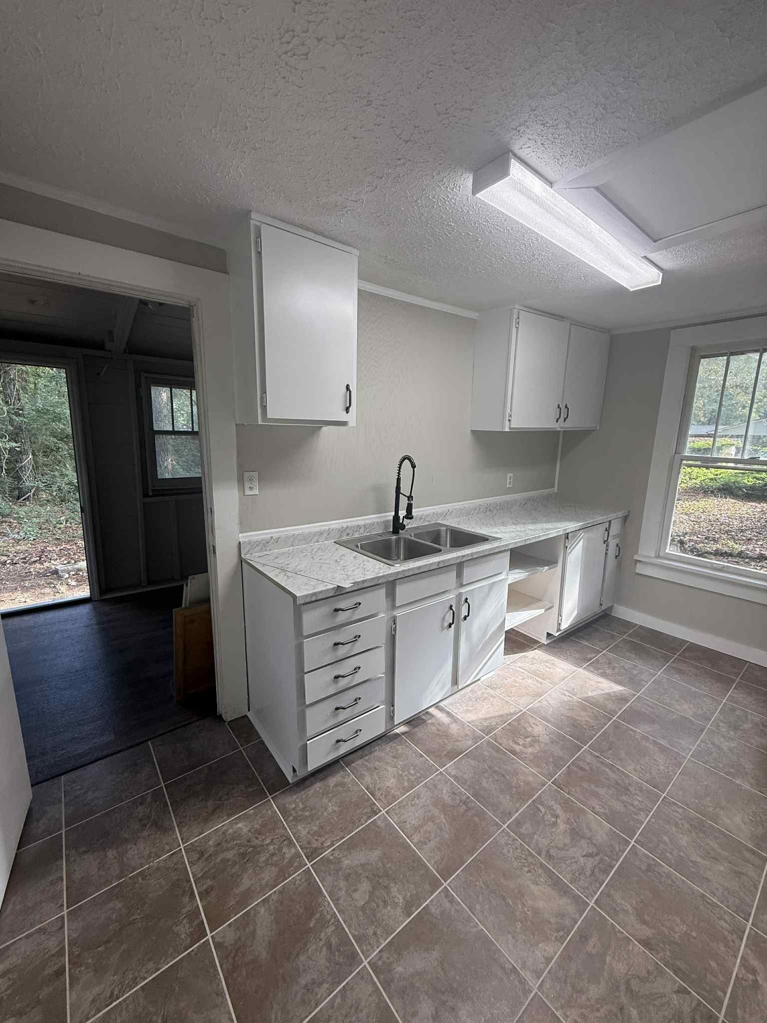 Kitchen with white cabinets, sink, and open doorway to an outside area. Brown tile floor.