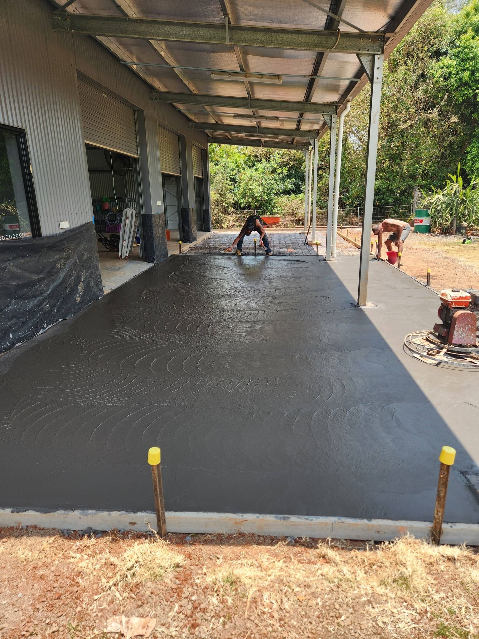 A Person Smoothing Wet Concrete on a Long, Covered Patio — Sun Co Concrete And Construction in Dimbulah, QLD