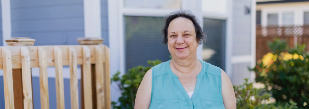 Older woman stands outside a house