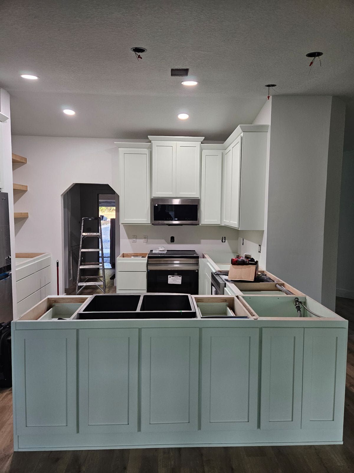 A bright, modern kitchen features white cabinetry, a large central island with seating, stainless appliances, and pendants.