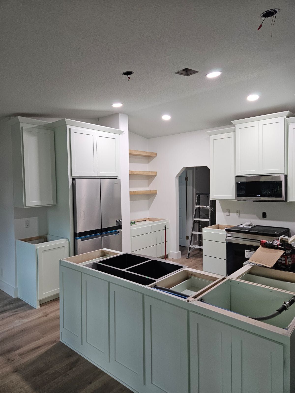 A bright, modern kitchen features light grey cabinets, marble countertops, an island, and gold pendant lighting.