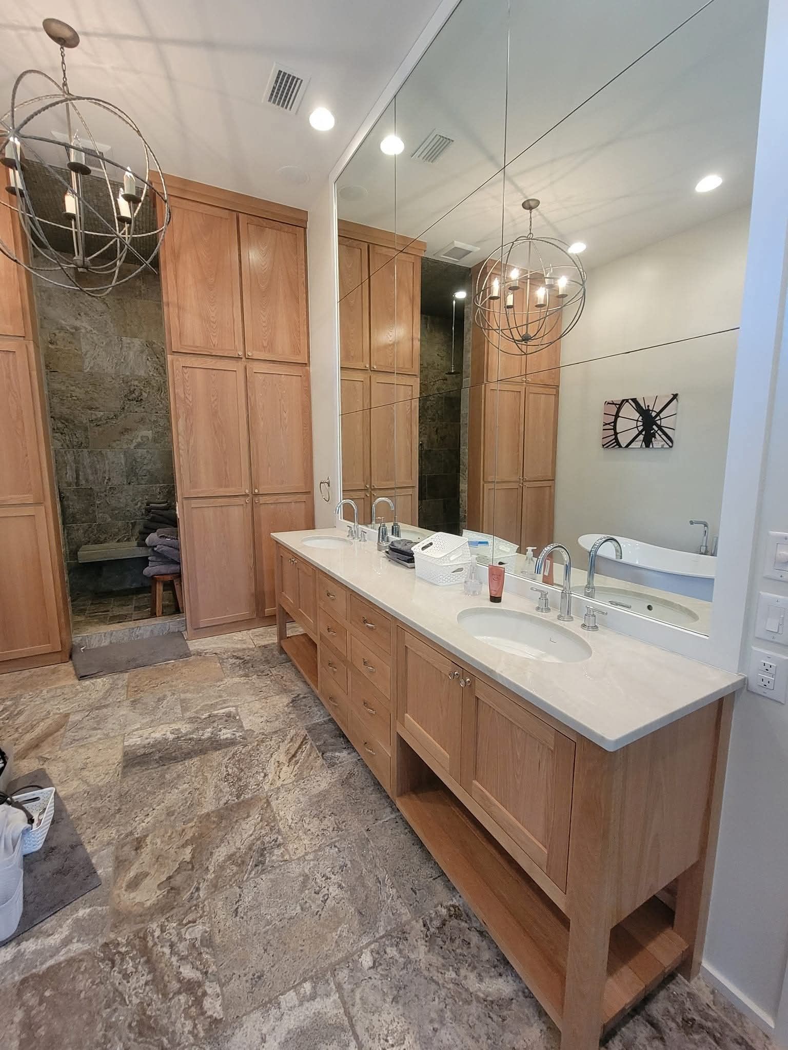 A modern bathroom with a light wood vanity, white stone countertop, two mirrors, and a glass-enclosed walk-in shower.