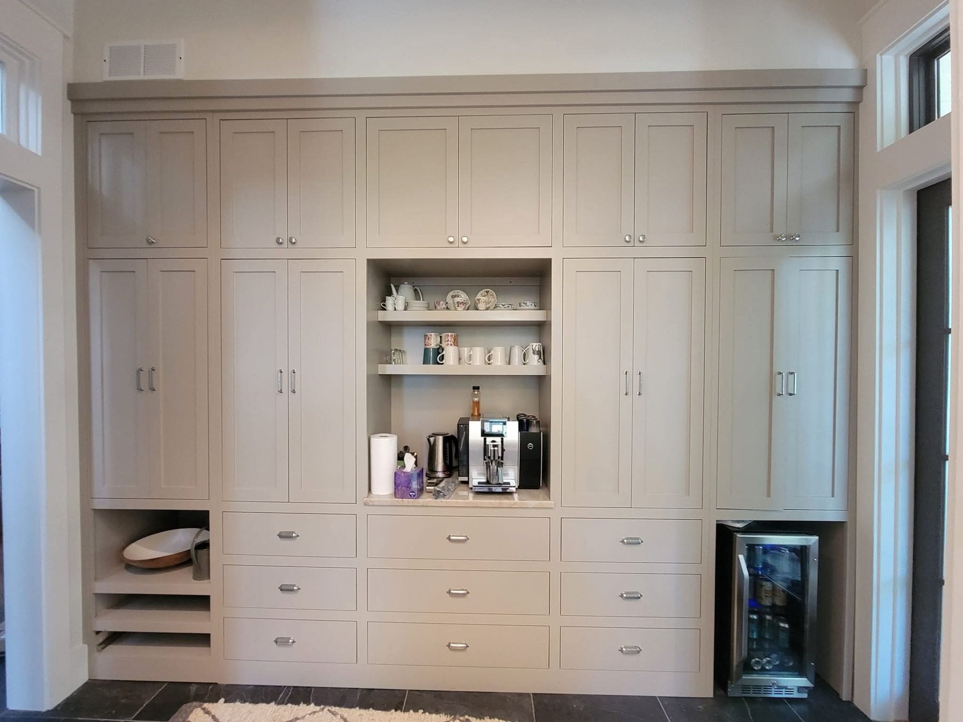 Custom wooden staircase storage unit with built-in drawers and cabinets, positioned next to a closed wooden entrance door.
