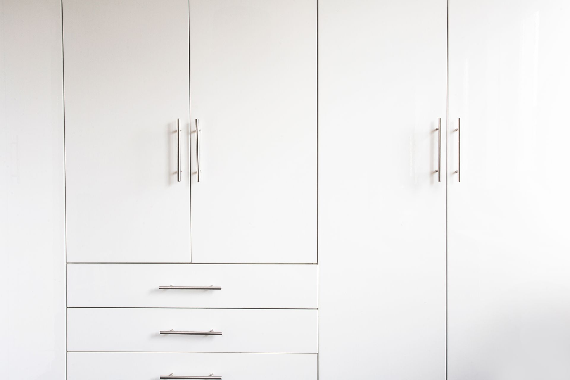 Modern white wardrobe with two doors, three drawers, and silver handles on a plain background.