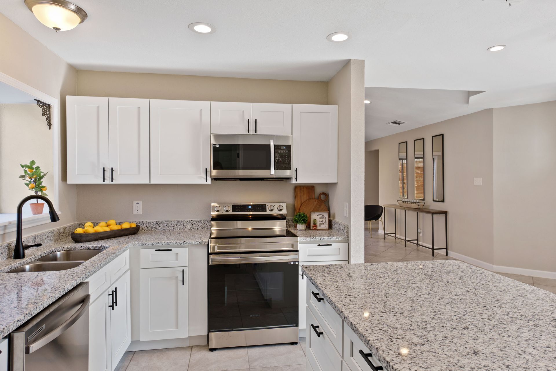 A modern, well-lit kitchen with white cabinets, speckled granite countertops, and stainless steel appliances.
