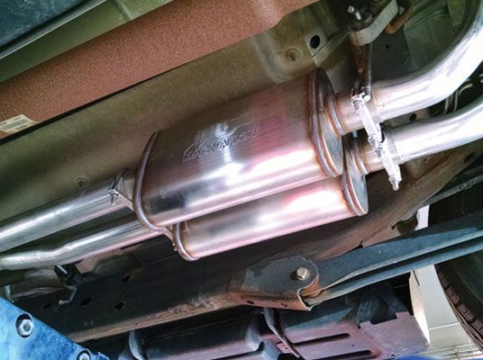 Undercarriage view of a vehicle's exhaust system featuring a dual muffler in a garage | Redline Automotive