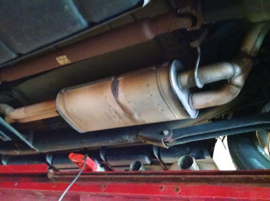 Undercarriage view of a car's exhaust system. Rust-colored pipes and muffler are visible | Redline Automotive