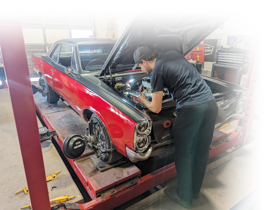 Mechanic working on a classic red car on a lift; garage setting | Redline Automotive