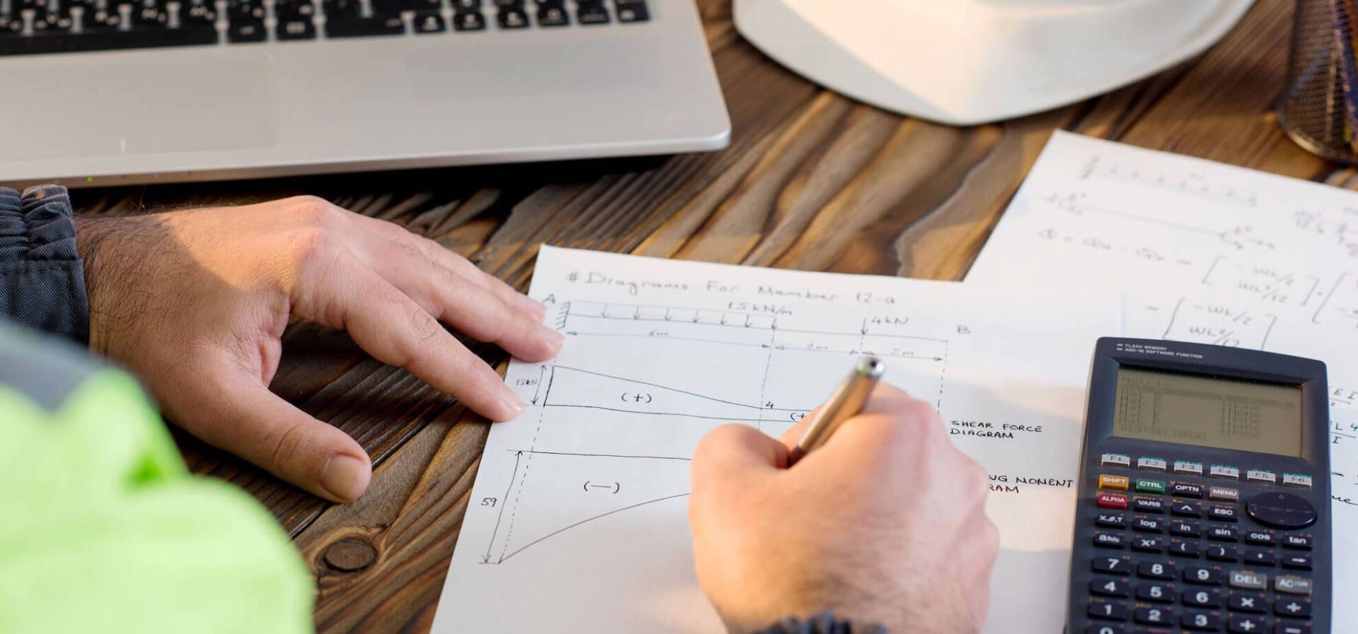 Un homme est assis à une table en bois et utilise une calculatrice et écrit sur un morceau de papier.