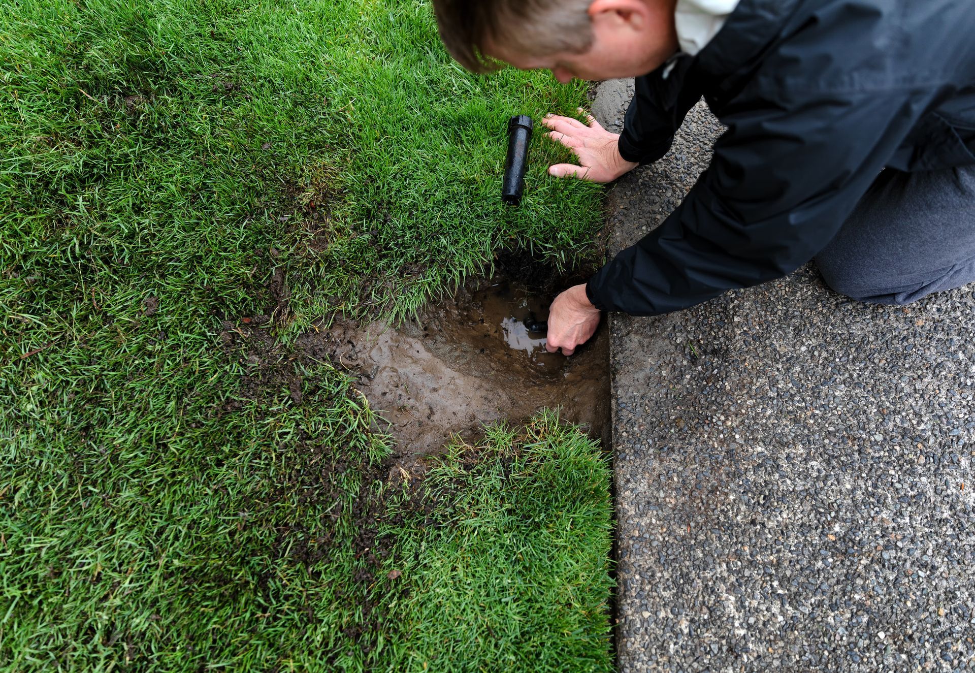 A lawn sprinkler system repair contractor performing repairs, with parts laying on the ground.