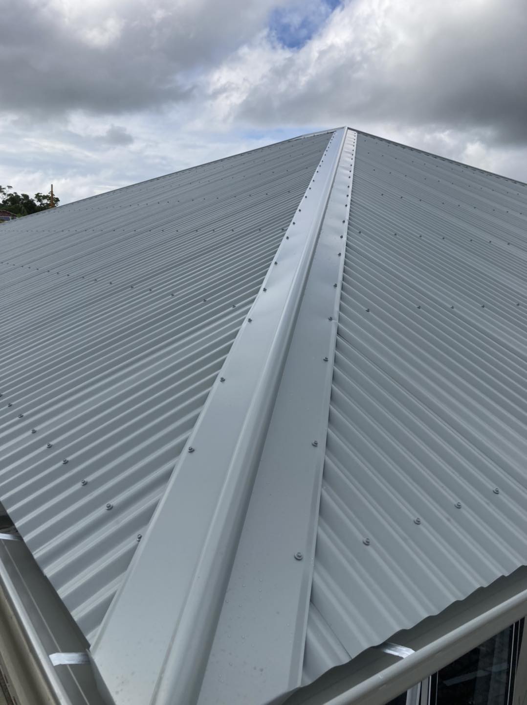 A close up of a metal roof with a gutter on a cloudy day.