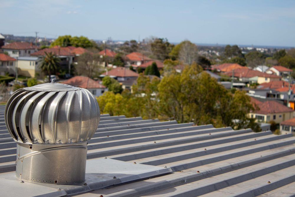 A roof with a stainless steel exhaust fan on it.