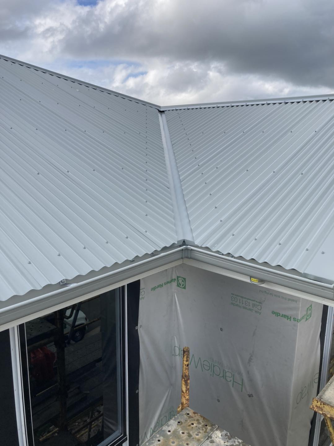 A white corrugated metal roof is being installed on a house.