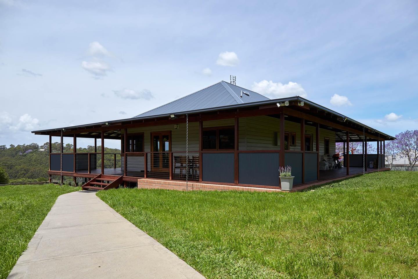 A large house with a large porch is sitting on top of a lush green hill.
