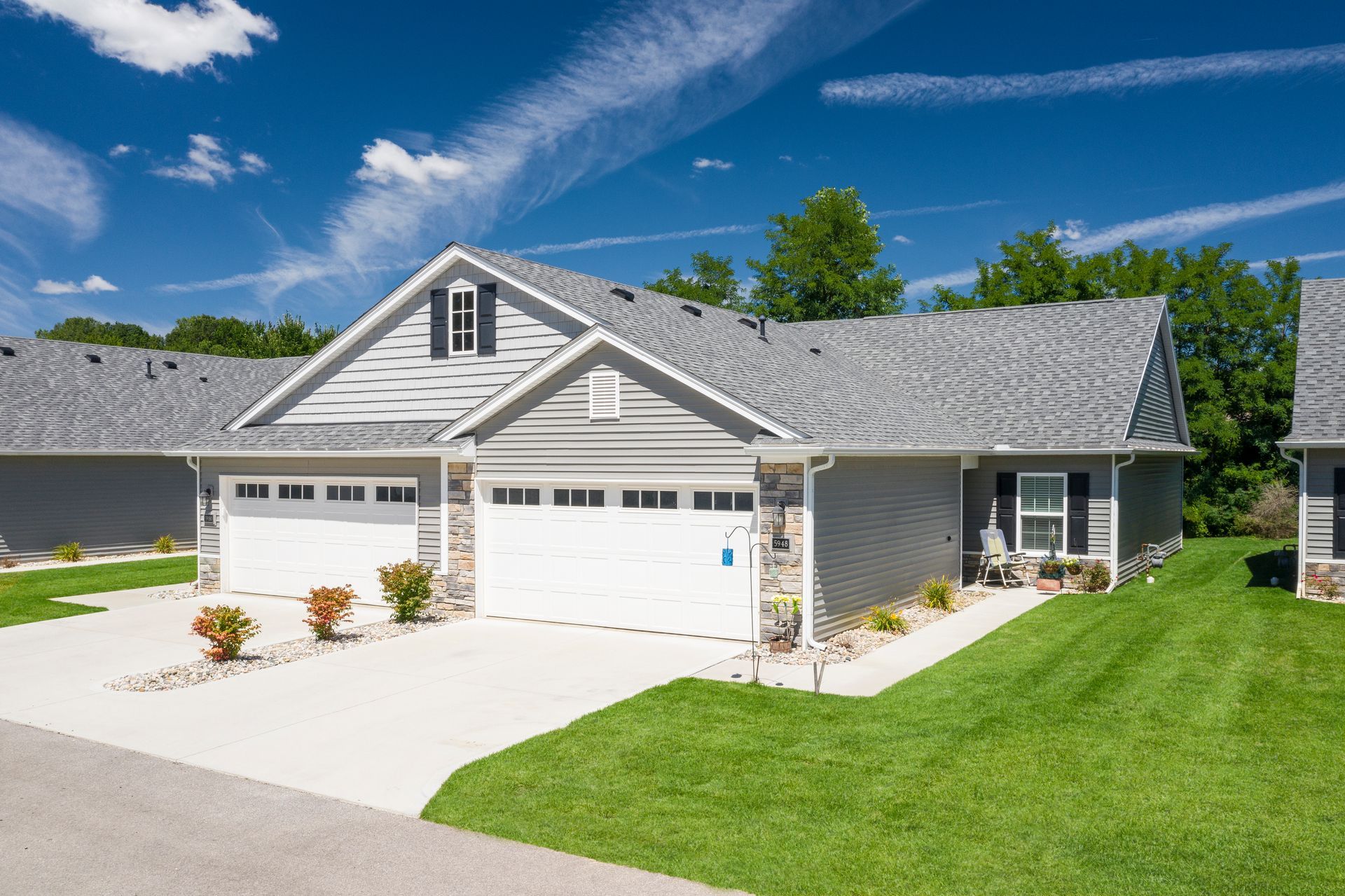 Photo of a duplex, with garages and driveways in the front and trees in the back