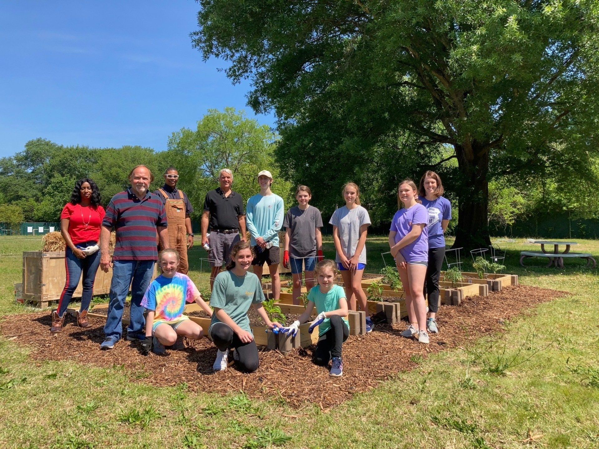 Group of people posing by a raised garden bed outdoors on a sunny day.