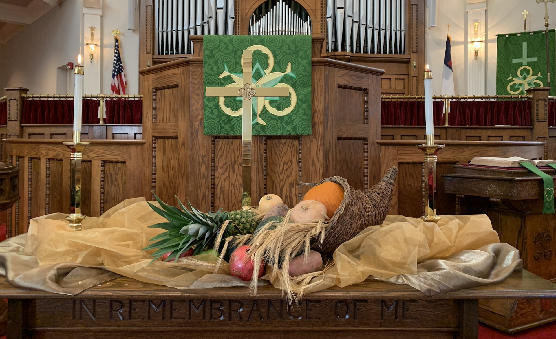 The communion table decorated with a cornucopia of fall harvest items, a cross, and an embroidered green banner.
