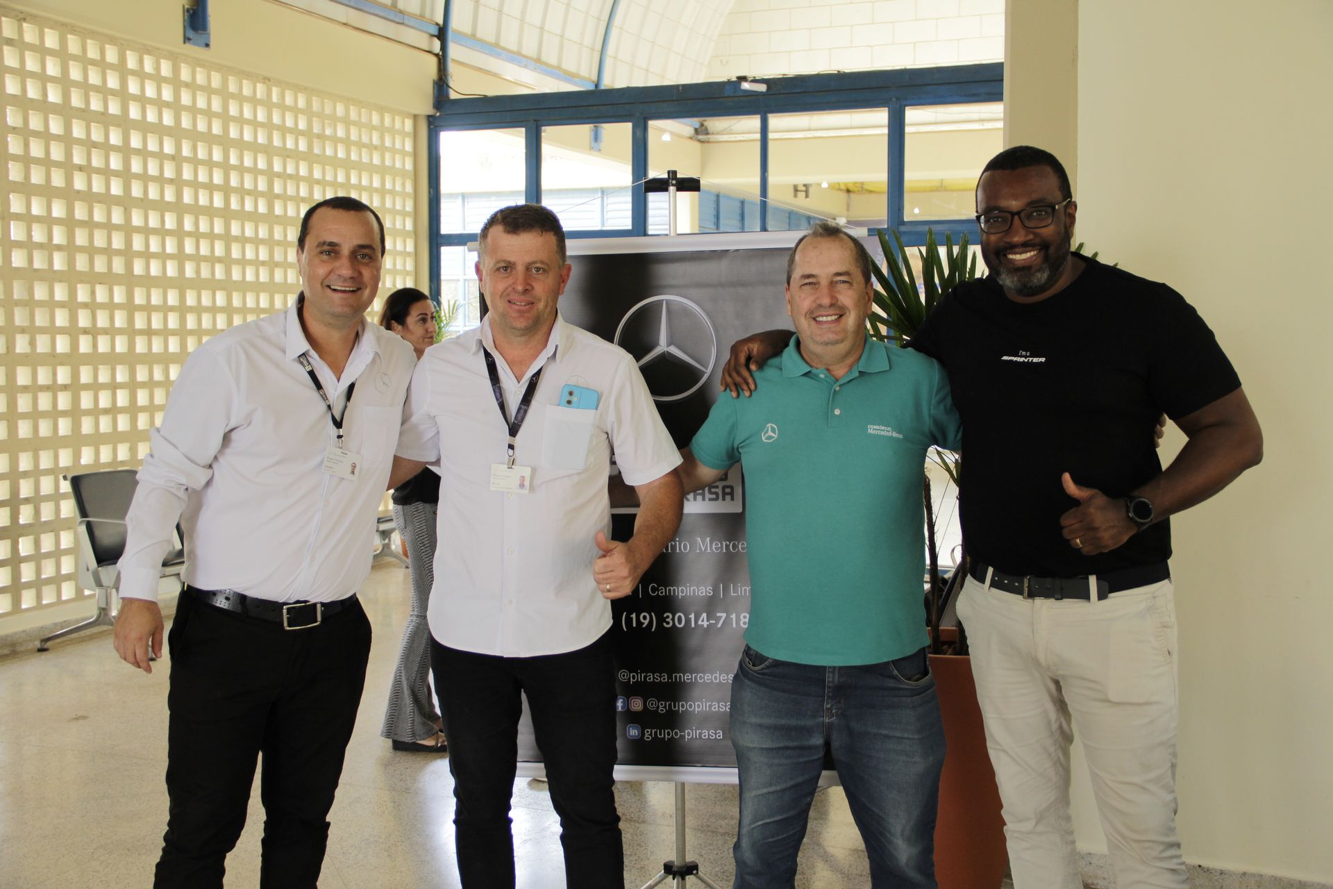 Four men pose together in a bright outdoor setting; one gives a thumbs-up.