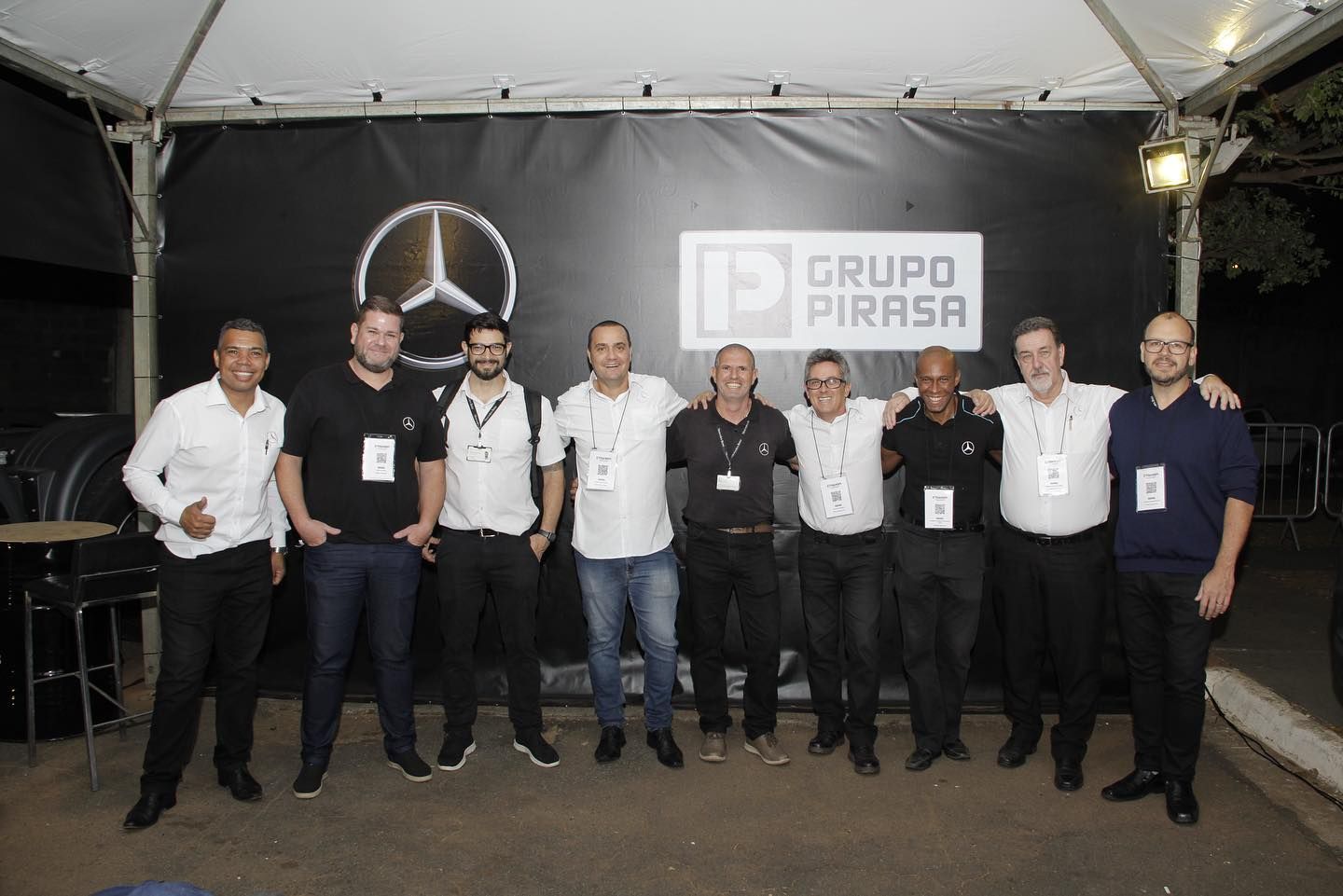 Group of men posing in front of a Mercedes-Benz and Grupo Pirasa backdrop; smiling and wearing name tags.