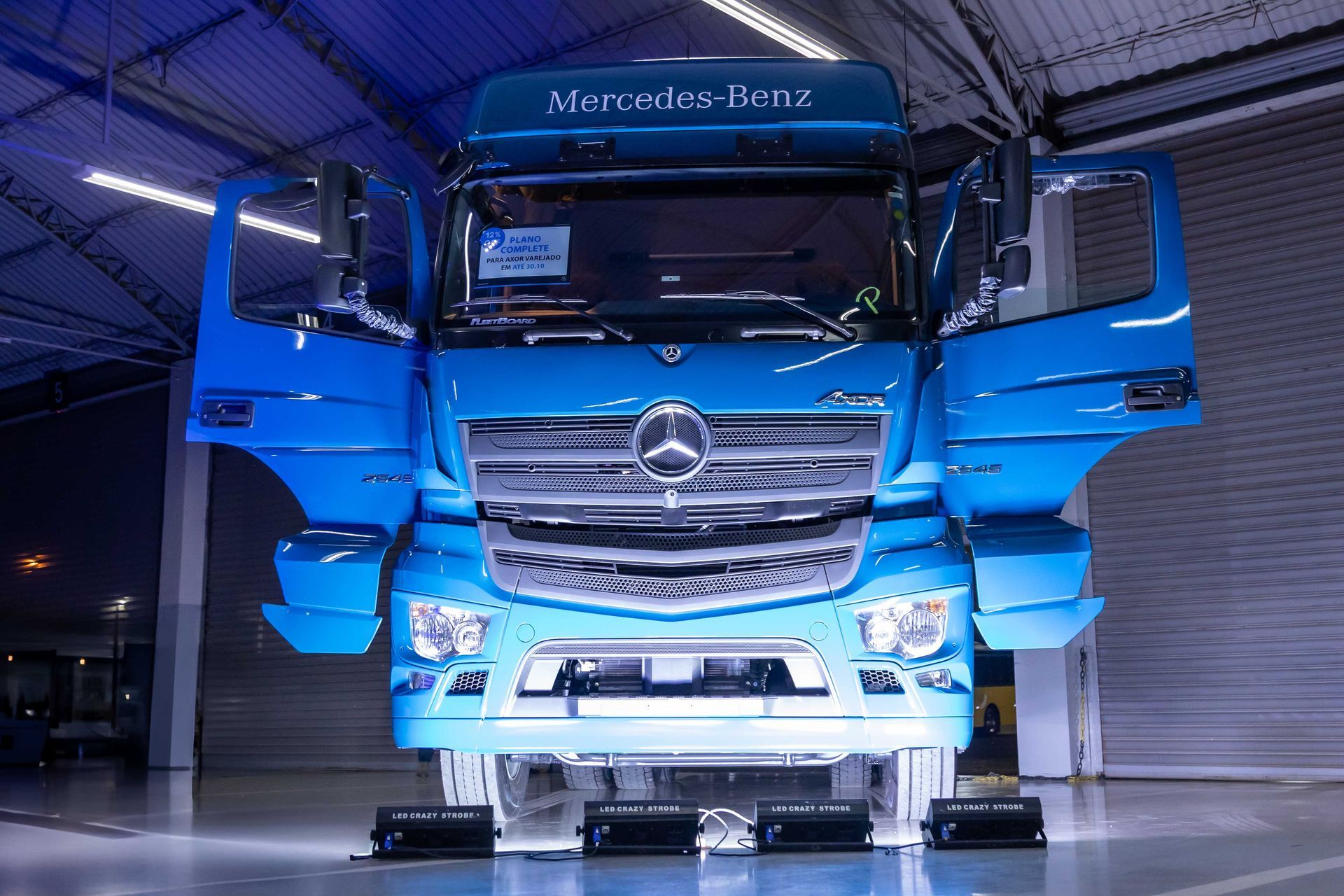 Blue Mercedes-Benz semi-truck with open doors in a warehouse, front view, illuminated.