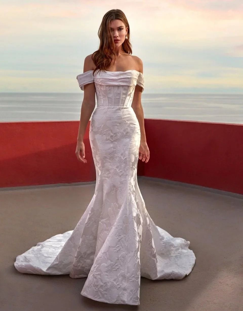 Woman in a white mermaid gown standing on a rooftop at sunset.