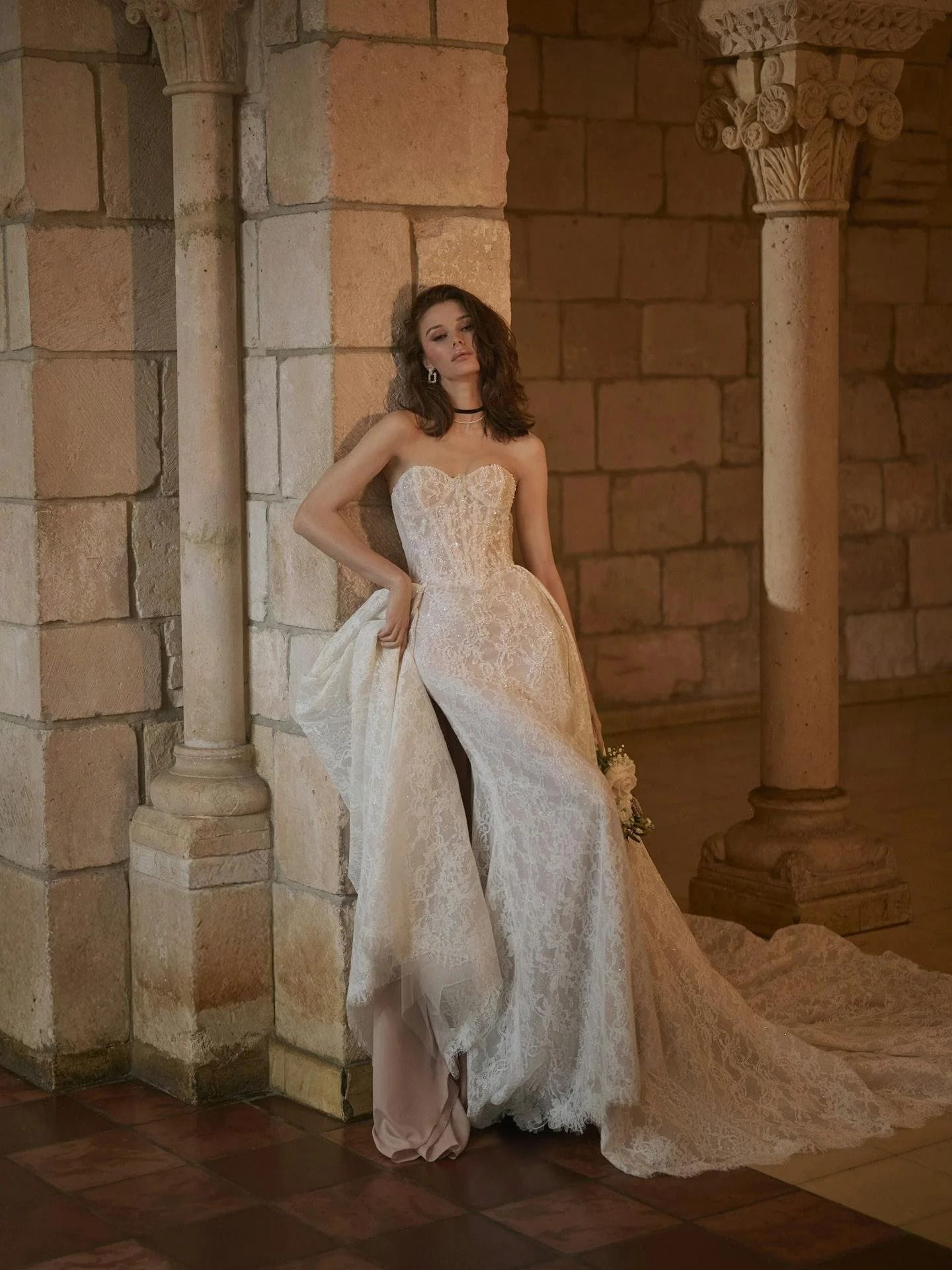 Woman in a white lace gown posing in an ornate stone corridor
