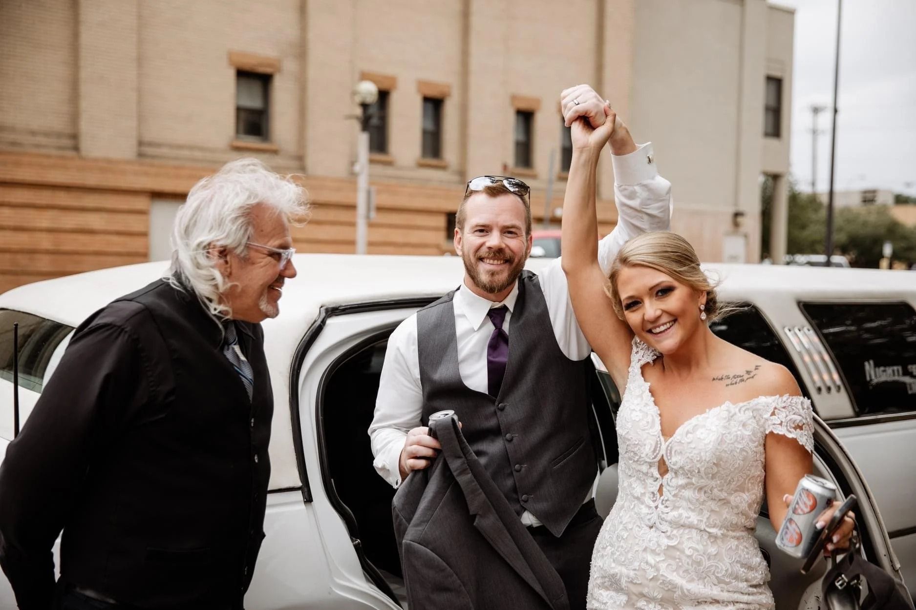 Wedding couple stepping out of a white limousine, smiling and celebrating outside a building.