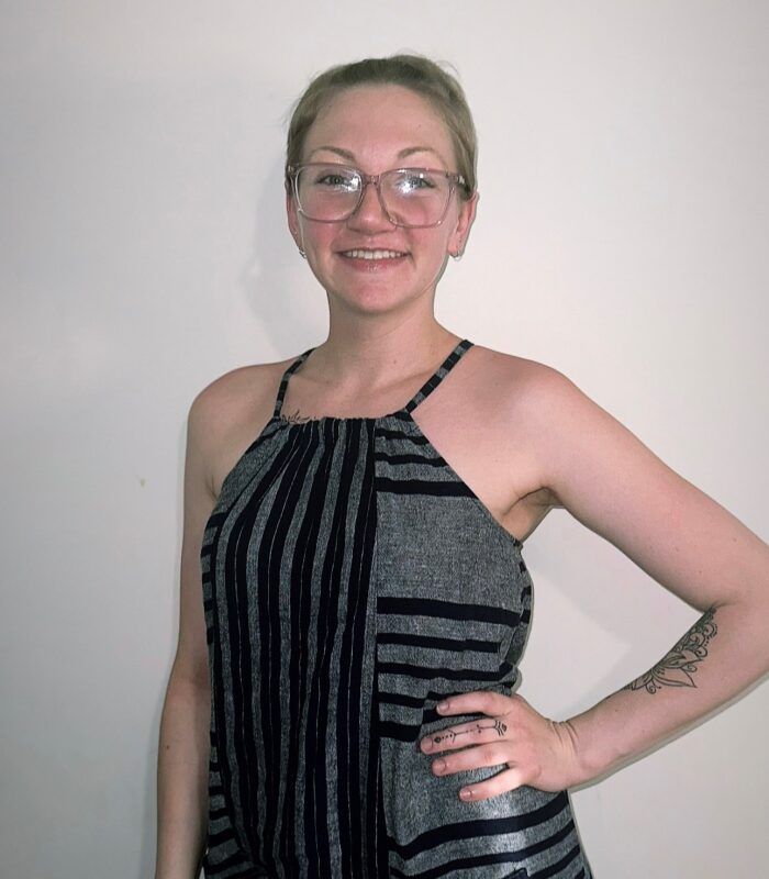 A woman wearing glasses and a striped top stands with her hand on her hip