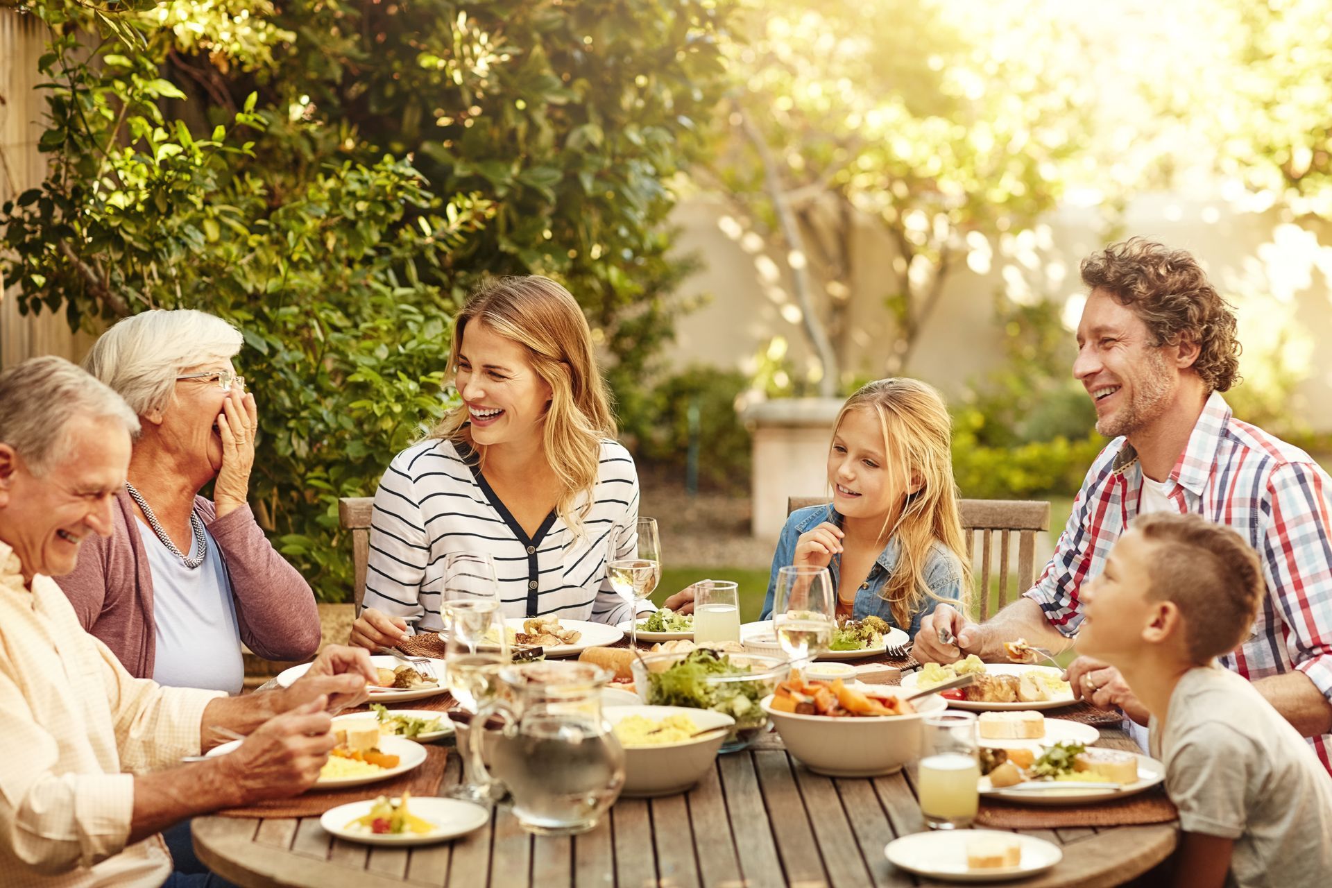 A large family is sitting at a table eating food.