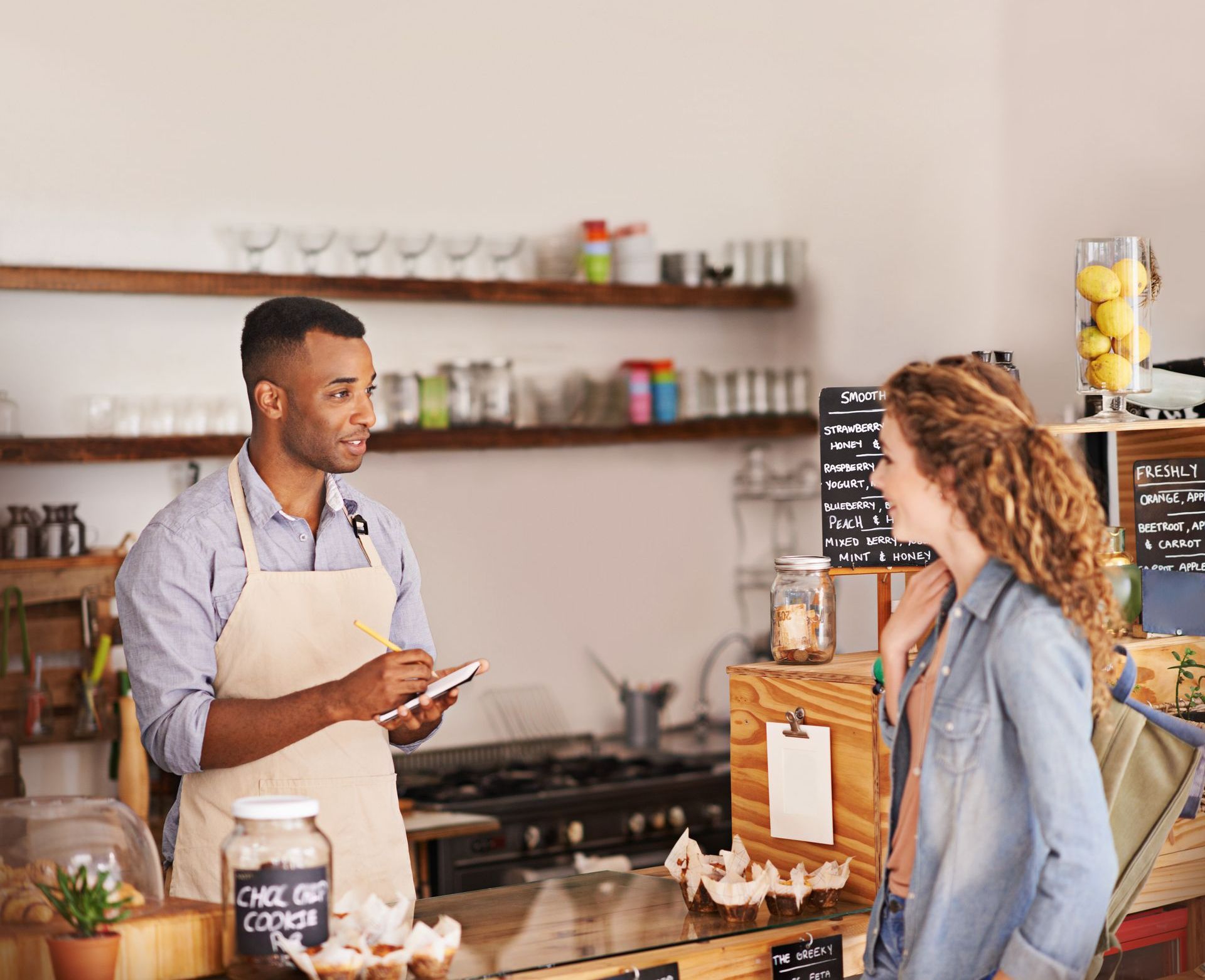 A man is talking to a woman in a restaurant while holding a tablet.