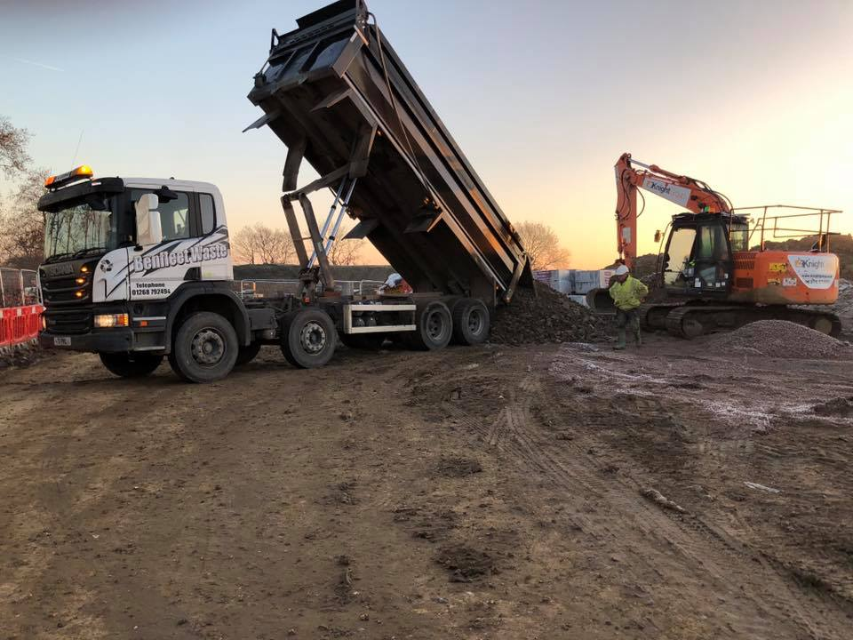Truck dumping gravel, excavator to the side, construction site at sunset.