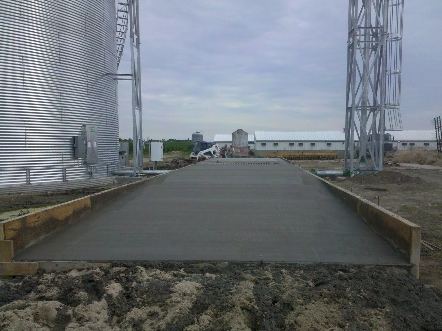 A concrete road is being built in front of a silo.