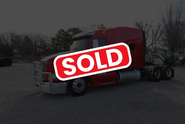 A red semi-truck with a large front grille guard parked outdoors, labeled with a red 