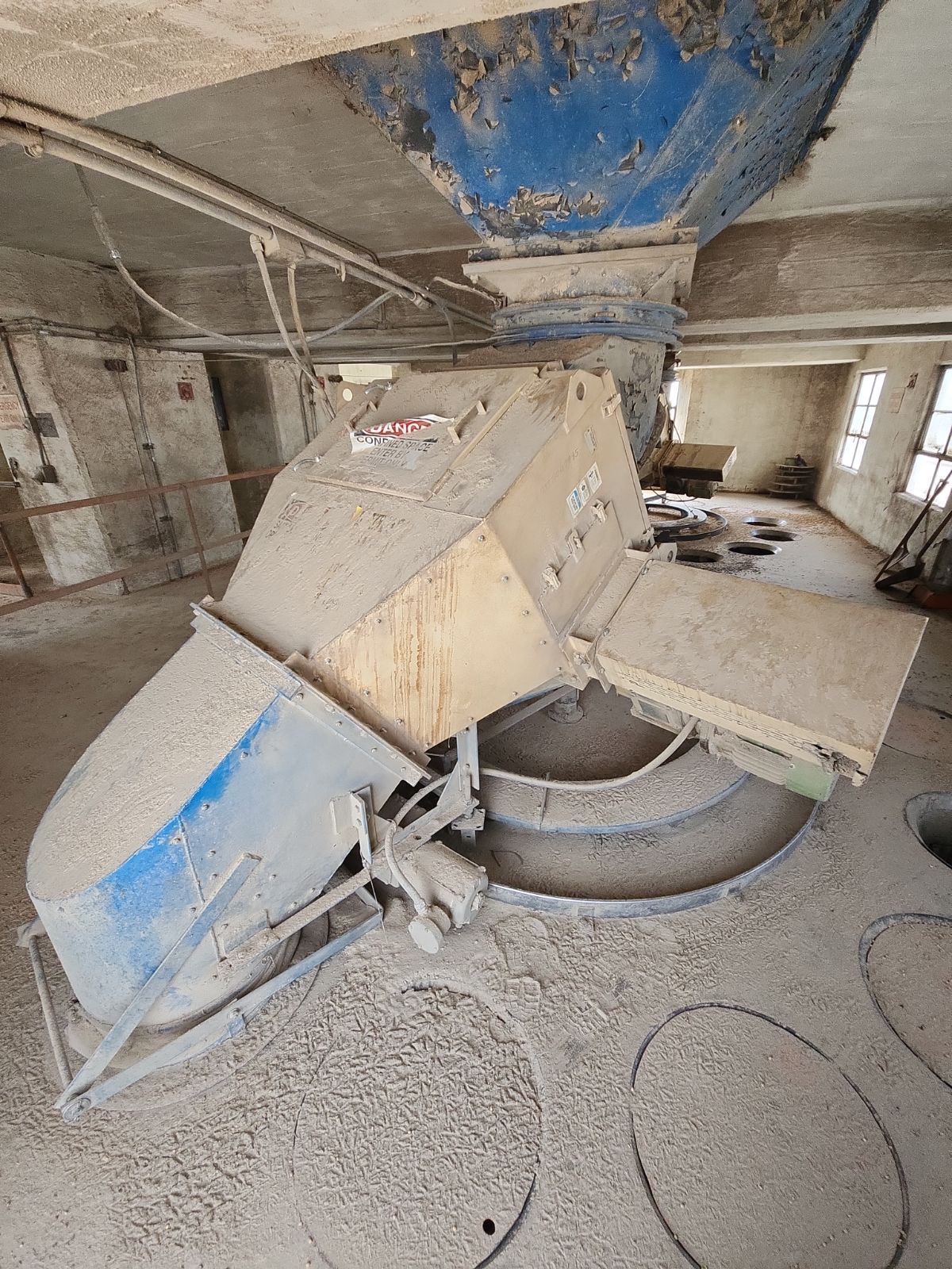 A machine is sitting in a dirty room with a blue pipe coming out of it.