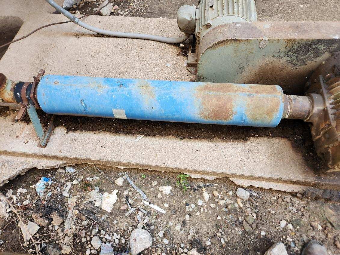 A blue pipe is laying on the ground next to a motor.