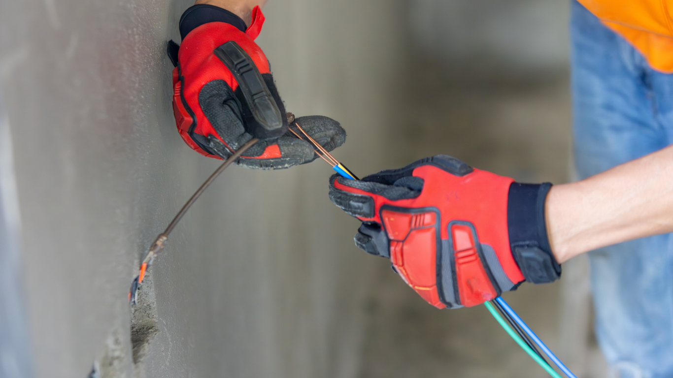 Hands in red gloves connecting electrical wires to a wall.