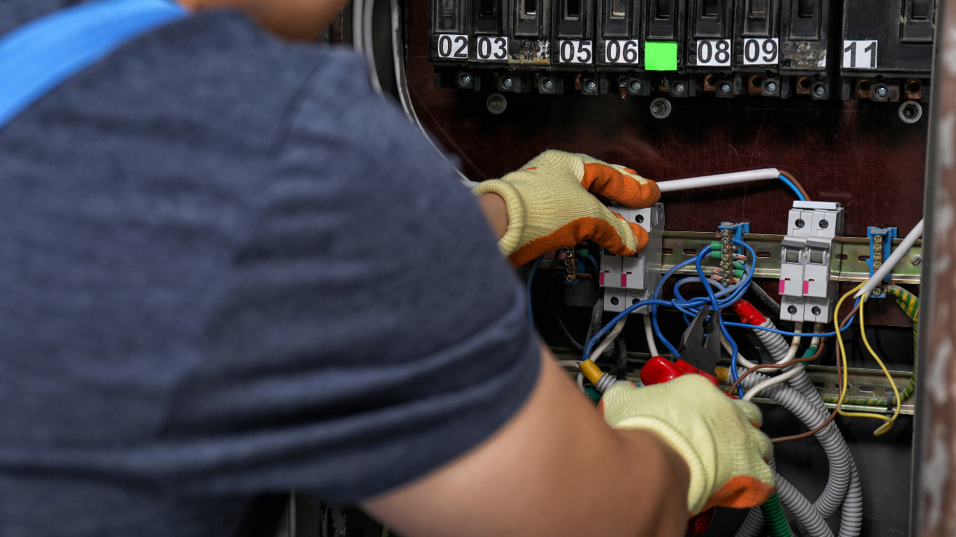 Electrician working on electrical panel, wearing gloves, with focus on wiring and circuits.