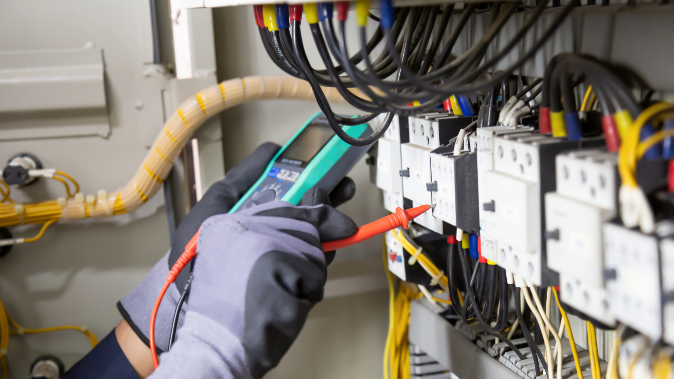 Person in gloves using a multimeter to test electrical connections in a control panel.